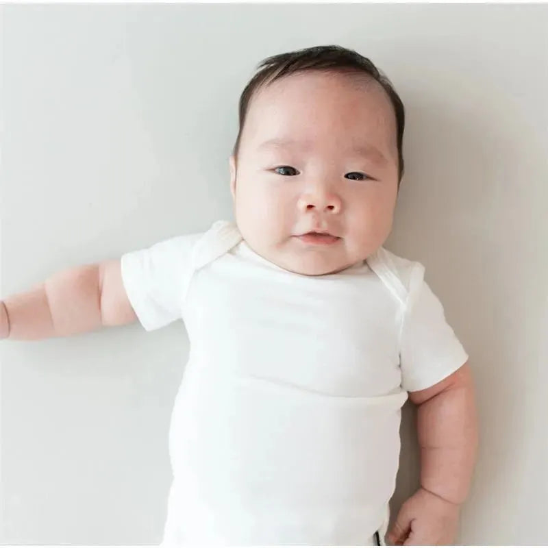 Baby wearing a white Kyte Baby bodysuit, lying on a light-colored surface, smiling at the camera.