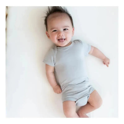 Smiling baby wearing a light gray, short-sleeve bodysuit, lying on a white surface.