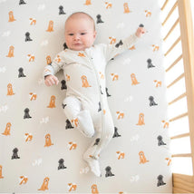 Baby in a zippered footie featuring fluffy dog patterns, lying on a crib mattress with cartoon dog prints.