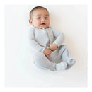 Neutral zippered footie in storm grey on a smiling baby seated against a white background.