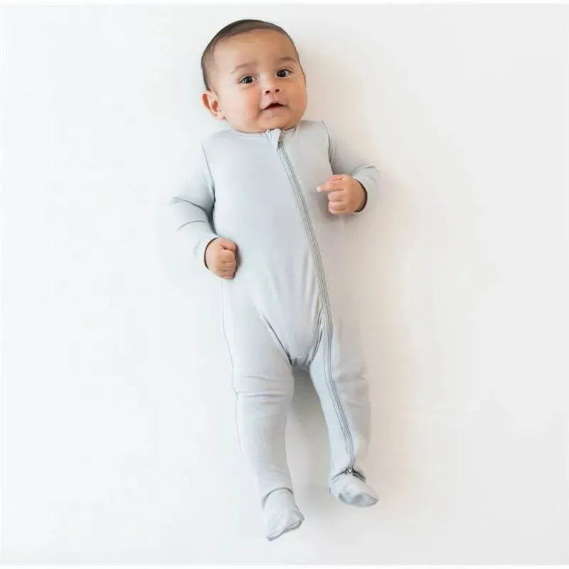 Neutral gray zippered footie for babies, displayed on an infant who is smiling and posing on a light background.