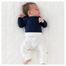 Baby wearing a navy long-sleeve shirt and white Kyte Baby pants, lying on a light background.