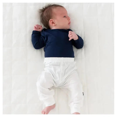 Baby wearing a navy long-sleeve shirt and white Kyte Baby pants, lying on a light background.