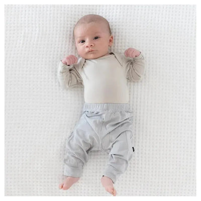 Baby wearing Kyte Baby Storm Pants, resting on a white textured blanket, with a light-colored long-sleeve shirt.