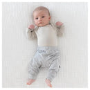 Baby wearing Kyte Baby Storm Pants, resting on a white textured blanket, with a light-colored long-sleeve shirt.