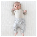 Gray baby pants from Kyte Baby are worn by an infant lying on a textured white blanket, looking curiously at the viewer.