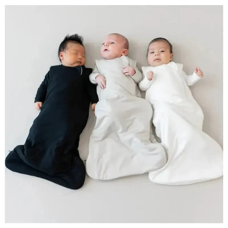 Three babies resting in bamboo sleep bags: one black, one grey, and one white, on a light background.
