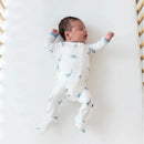 Zippered footie for babies featuring blue dinosaur prints, worn by an infant lying on a white crib mattress.