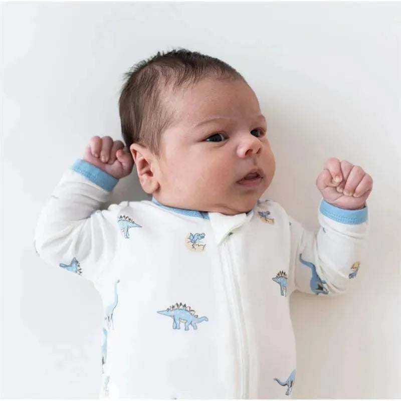 Baby wearing a white zippered footie with dinosaur prints in blue tones, lying on a light background.