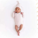Bamboo baby knotted cap in blush color on a sleeping infant, dressed in a matching soft onesie, posed on a white background.