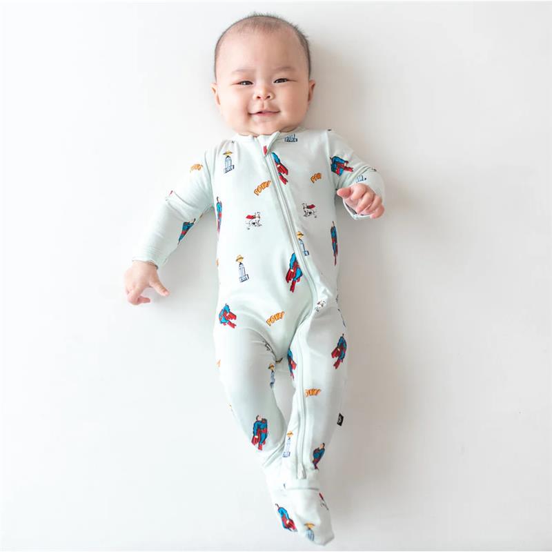 Kyte Baby bamboo zippered footie in Superman design, featuring playful graphics, worn by a smiling baby on a light background.