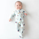 Kyte Baby bamboo zippered footie in Superman design, featuring playful graphics, worn by a smiling baby on a light background.
