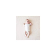 A baby lies on a light-colored surface, smiling while wearing a white Kyte Baby bodysuit.