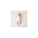 A baby lies on a light-colored surface, smiling while wearing a white Kyte Baby bodysuit.