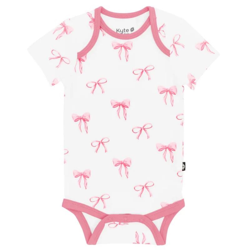 Kyte Baby bodysuit featuring a white background adorned with pink bow patterns and pink trim around the neckline and legs.