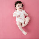 Infant wearing a white bodysuit with pink bow prints, smiling on a pink background.