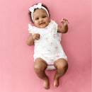 Kyte Baby Bubble Romper In Bow worn by a smiling infant, features a white fabric with pink bows and ruffled sleeves.