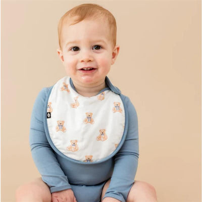 A smiling toddler wearing a blue long-sleeve onesie and a white bib featuring teddy bear prints.