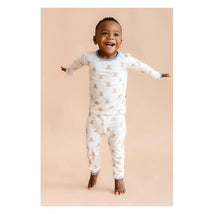 Smiling child wearing Kyte Baby long sleeve pajamas with teddy bear print, standing with arms outstretched against a light background.