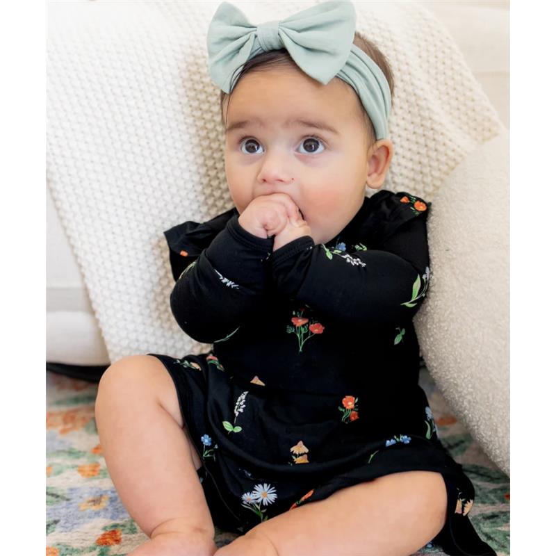 Baby sitting on a rug, wearing a black long sleeve twirl bodysuit dress with colorful floral patterns and a mint green headband.