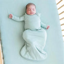 Bamboo sleep bag in sage color, worn by a peacefully sleeping baby, lying on a light blue crib mattress.