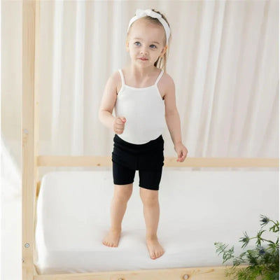 Ribbed spaghetti strap bodysuit in cloud color worn by a toddler standing on a bed with a wooden frame.