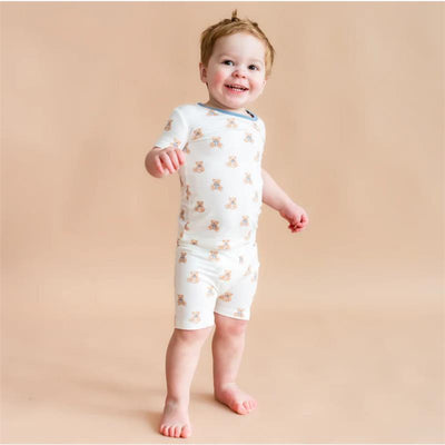 Toddler wearing Kyte Baby short sleeve pajamas featuring a teddy bear print, smiling against a neutral background.