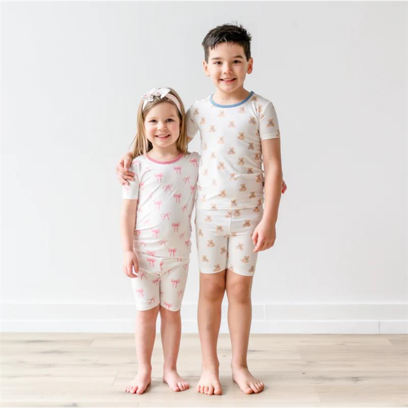 Younger girl in pink pajama set with bows, older boy in white teddy bear pajamas, both smiling and standing together.