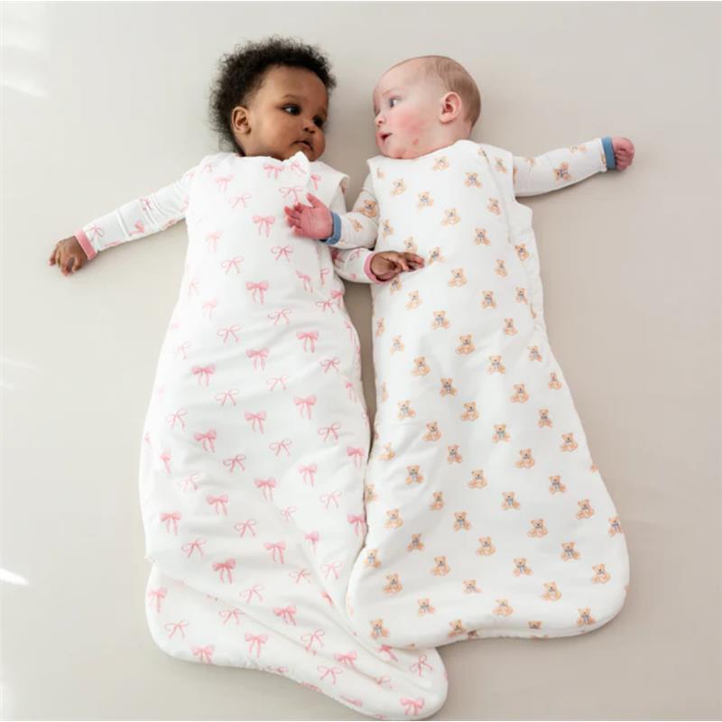 Two babies resting on a light surface, each in a Kyte Baby Sleep Bag; one features pink bows, the other has teddy bear prints.