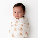 Infant swaddled in a Kyte Baby blanket featuring teddy bear prints, with a neutral background and a curious expression.