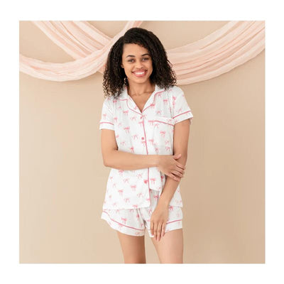 Women’s short sleeve pajama set featuring a white background with pink bow patterns, modeled by a smiling woman.