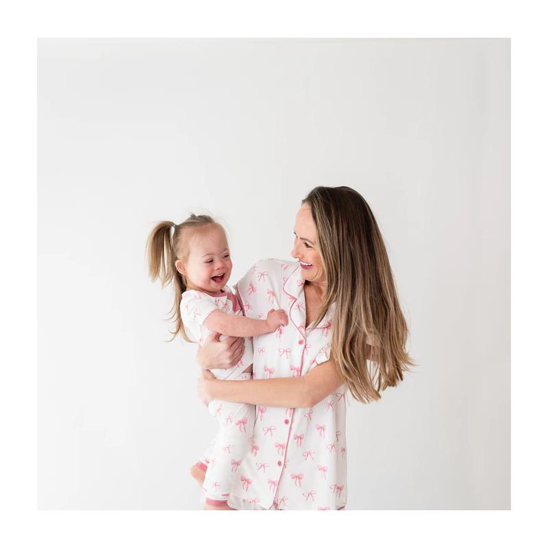 Mother and daughter joyfully interact, both wearing matching pink bow-patterned pajamas.