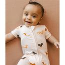 Smiling baby wearing a cream-colored shortall romper adorned with dachshund prints, lying on a neutral background.