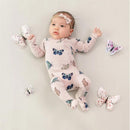 Zippered footie for infants in blush with colorful butterfly patterns, featuring a baby girl lying on a light background surrounded by butterfly toys.