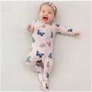 Smiling baby in a blush pink zippered footie covered in butterfly prints, lying on a light background.