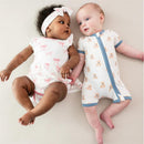 Infants lying on a light background; one wears a teddy bear zippered romper and the other in a pink bow dress.