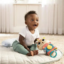 Baby sitting on a quilted mat, smiling excitedly while holding the Lamaze Arty Says Cheese toy, featuring a colorful design.