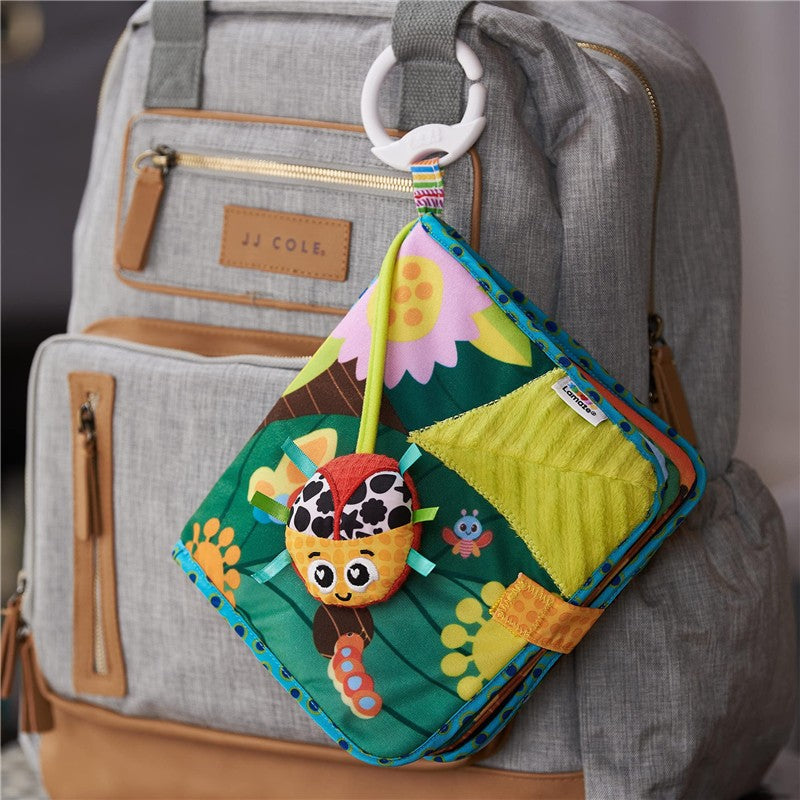 Colorful Lamaze Bitty Bug Soft Day Book attached to a backpack, featuring a smiling insect design and various textured fabrics.
