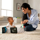 A smiling woman engages with a baby on the floor, showcasing the colorful Lamaze Caterpillar™ sensory book with various textures and patterns.