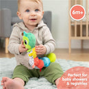 Toddler sits on a soft rug, smiling while holding a colorful Lamaze Fidget Fun Caterpillar toy, designed for ages 6 months and up.