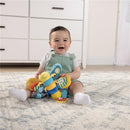 Infant sitting on a soft rug, smiling while playing with Lamaze Freddie the Firefly, a colorful plush toy.