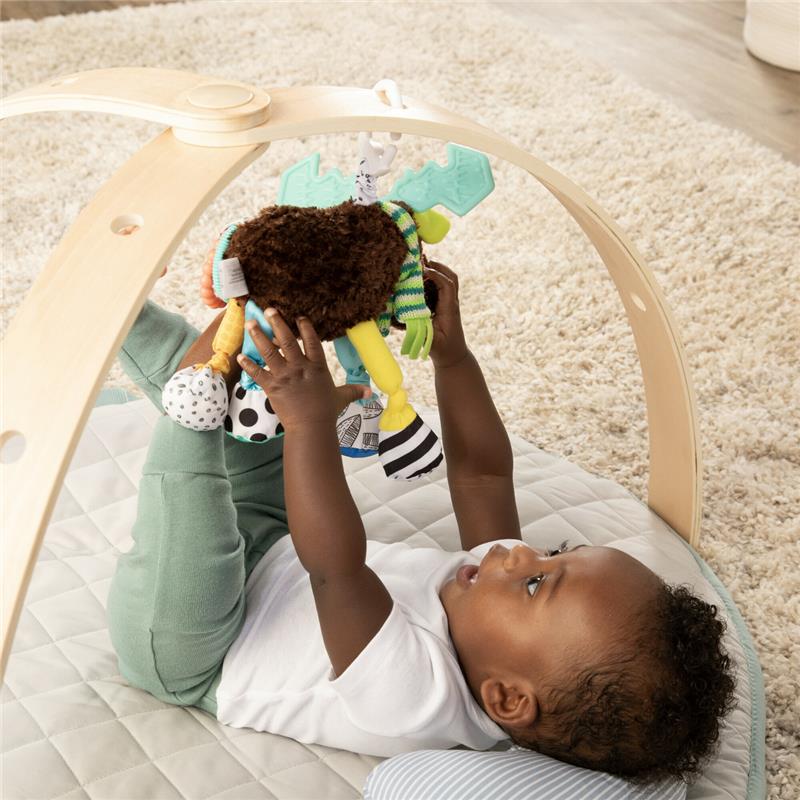 Baby reaching for Lamaze Mortimer The Moose Clip & Go toy, featuring colorful textures and shapes, while lying on a play mat.