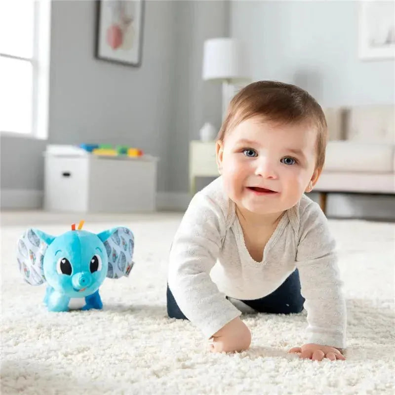 A smiling baby crawling on a carpet next to a blue Puffaboo Elephant sensory toy with colorful ears.