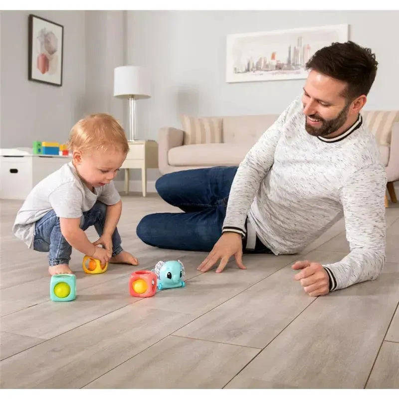 A toddler plays with colorful stacking blocks and a small elephant toy alongside a smiling adult on a wooden floor.