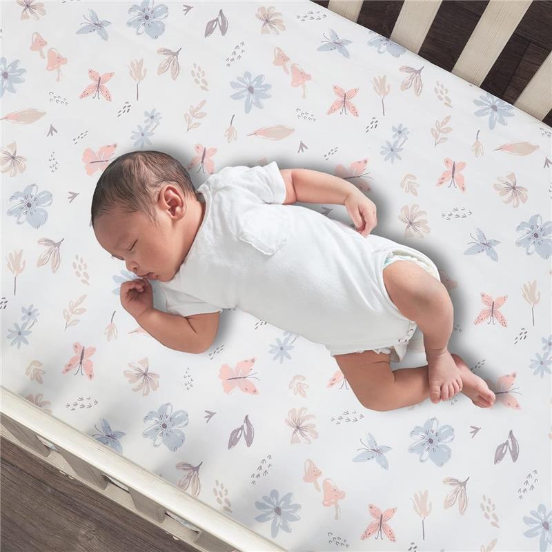 Baby lying on a floral and butterfly printed crib sheet featuring pastel colors on a crib mattress.