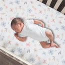 Baby lying on a floral and butterfly printed crib sheet featuring pastel colors on a crib mattress.