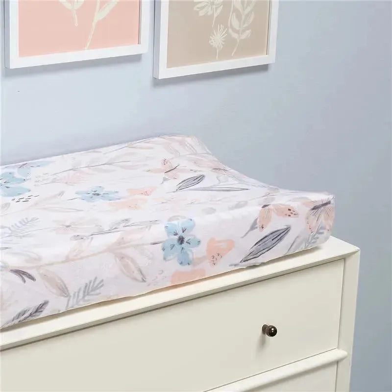 Soft changing pad cover featuring a watercolor floral and butterfly design in pastel colors, placed on a dresser.