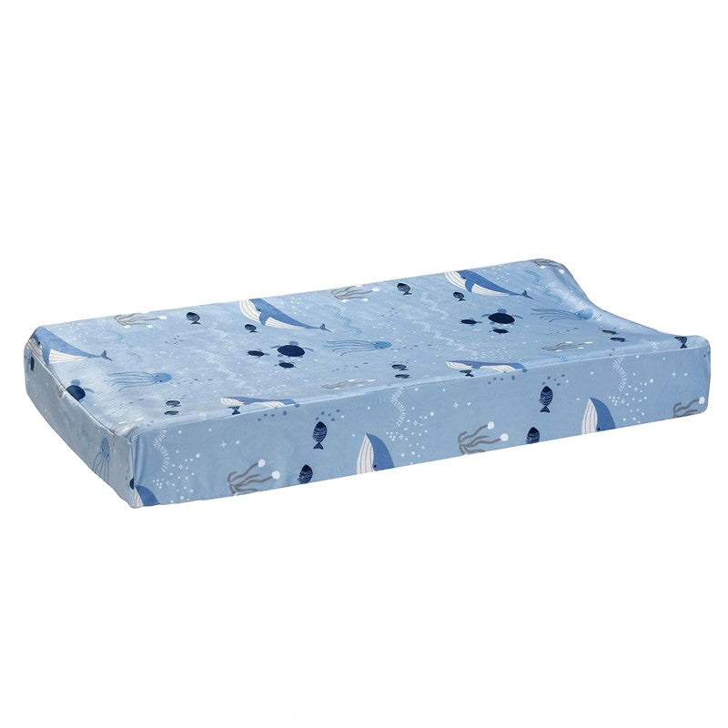 Changing pad cover featuring a light blue design with whales, fish, and ocean waves, ideal for baby changing stations.