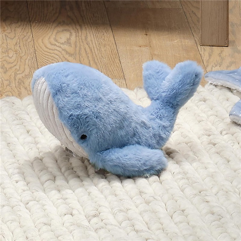 Plush blue whale toy from Lambs & Ivy, featuring a soft texture and a smiling face, resting on a woven rug.