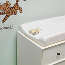 Changing pad cover featuring a whimsical illustration of Winnie the Pooh holding a blue blanket, displayed on a white changing table.